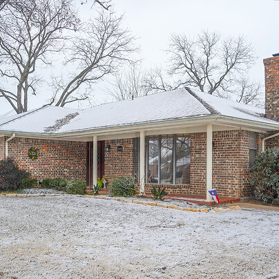 Snow-covered brick house with a front porch and winter scenery.